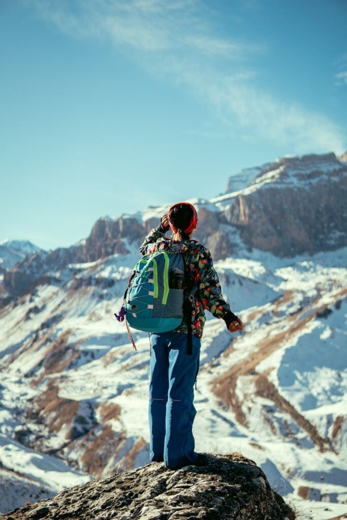 Person hiking in Qusar, Azerbaijan, admiring snowy mountains under clear blue sky.